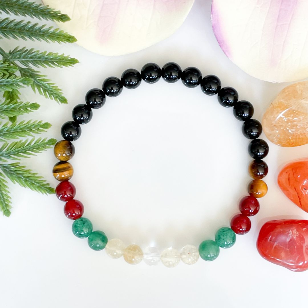 Multicolored beaded bracelet on a white surface with green leaves and stones.