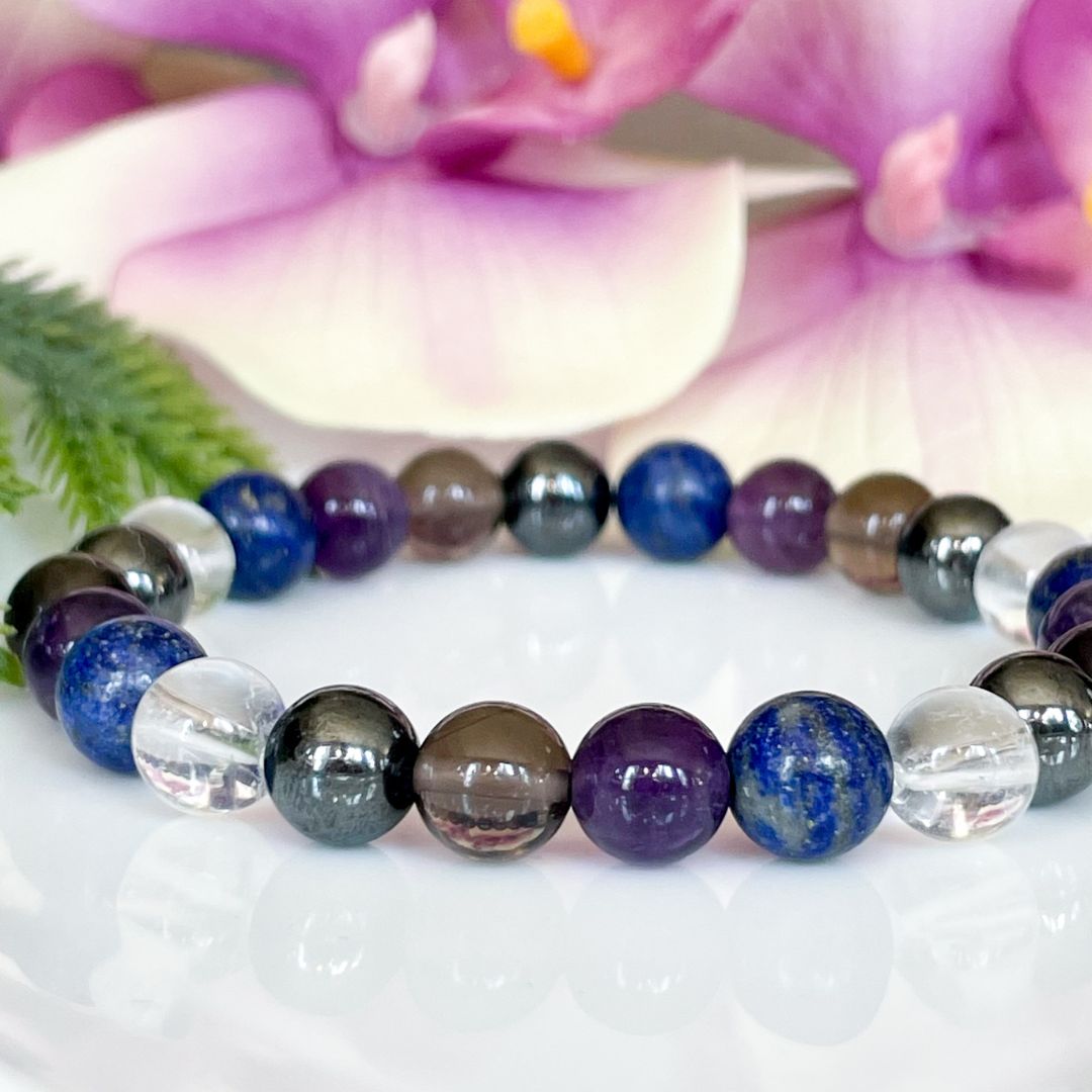 Multicolored beaded bracelet on a white surface with pink flowers in the background