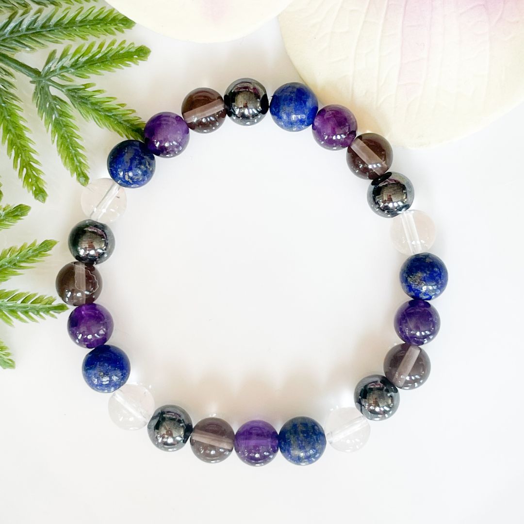 Multicolored beaded bracelet on a white surface with green leaves in the background
