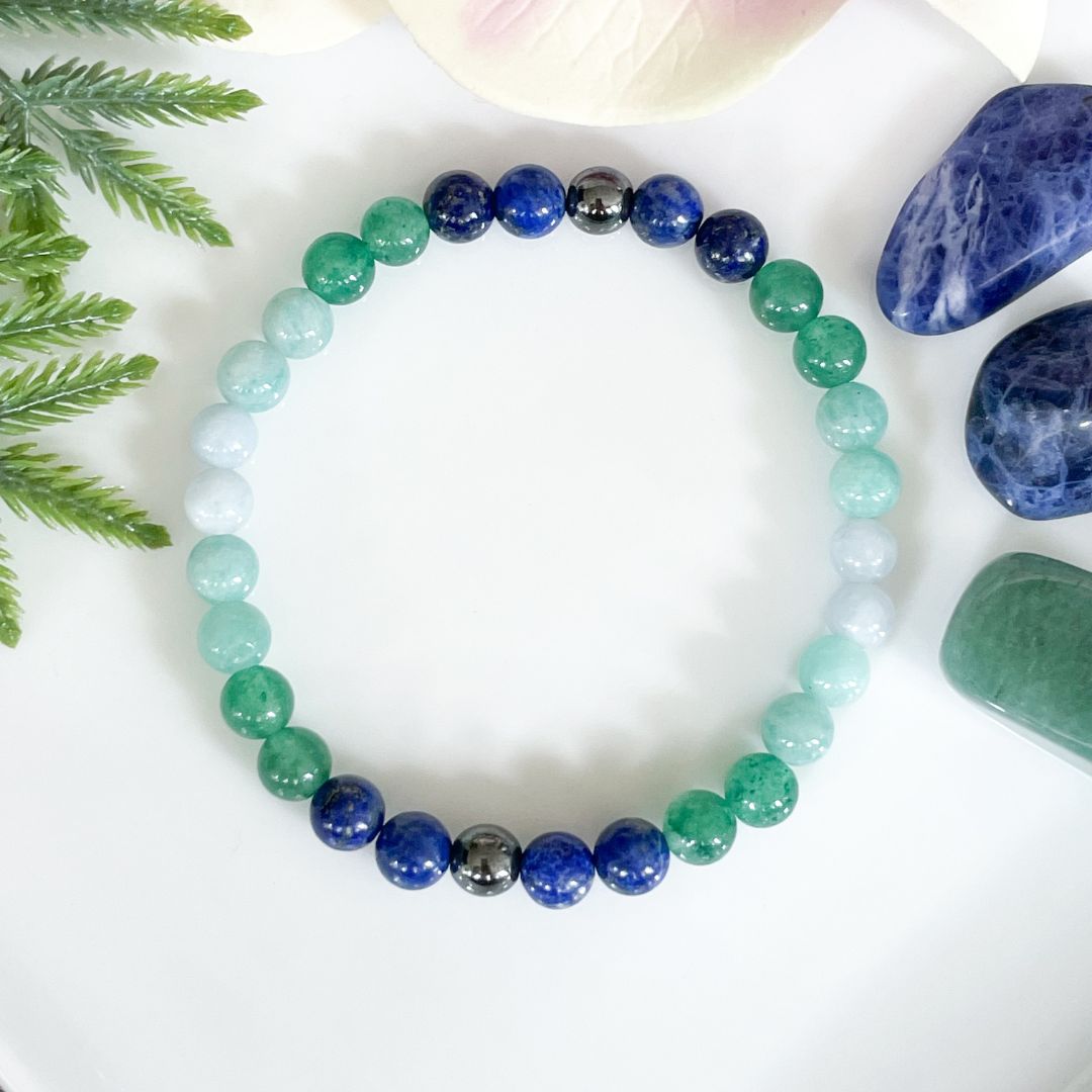 Beaded bracelet with green and blue beads on a white surface with stones and leaves.