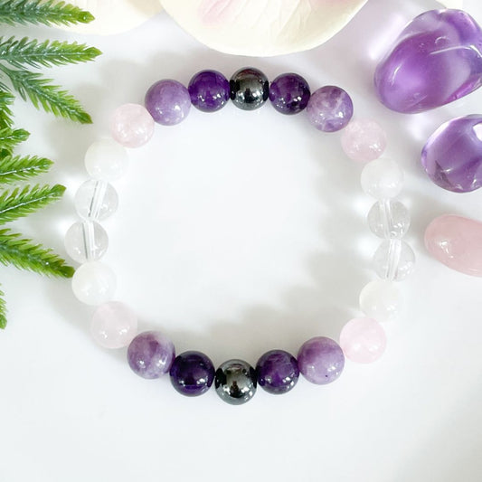 Virgo Beaded bracelet with purple, black, and white beads on a white surface with green leaves.