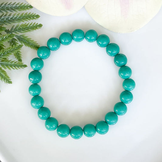 Turquoise beaded bracelet on a white surface with green leaves in the background