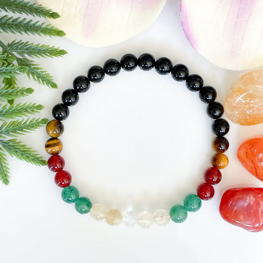 Multicolored beaded bracelet on a white surface with green leaves and stones.