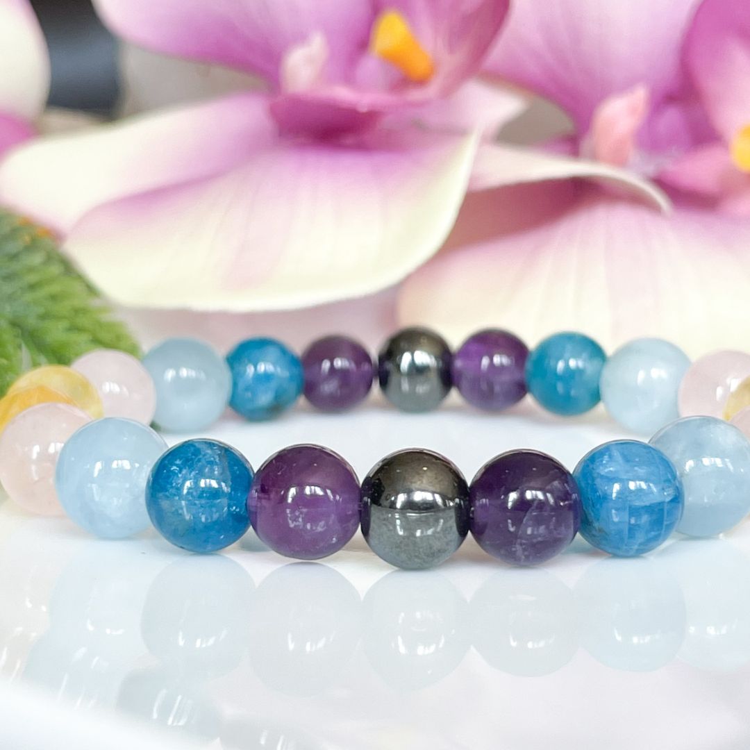 Multicolored beaded bracelets on a white surface with pink flowers in the background