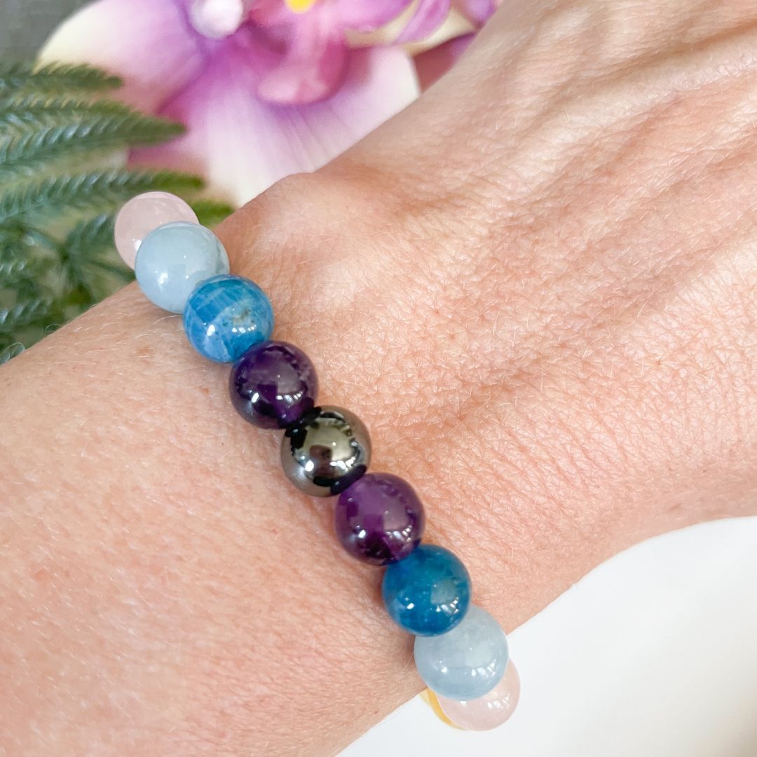 Beaded bracelet with multicolored beads on a wrist, with a blurred background of flowers and greenery.