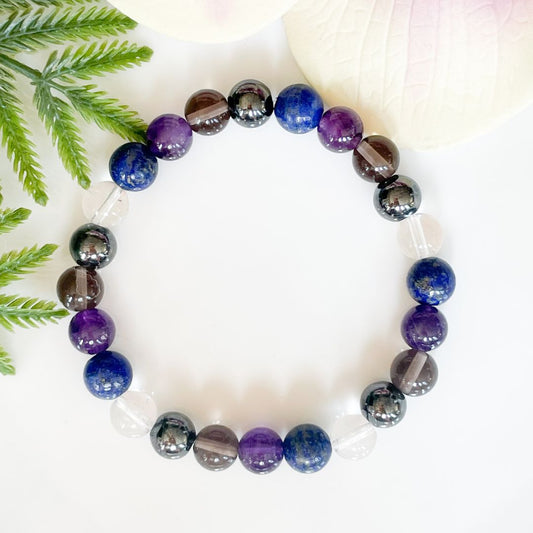 Multicolored beaded bracelet on a white surface with green leaves in the background