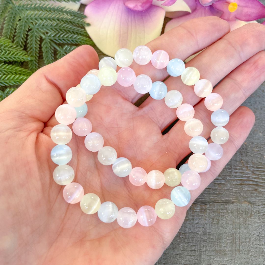Hand holding a stack of pastel-colored beaded bracelets with a floral background