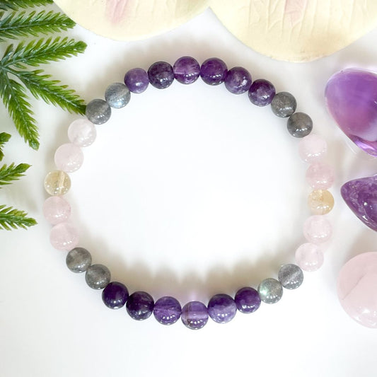 Multicolored beaded bracelet on a white surface with green leaves and a purple crystal.