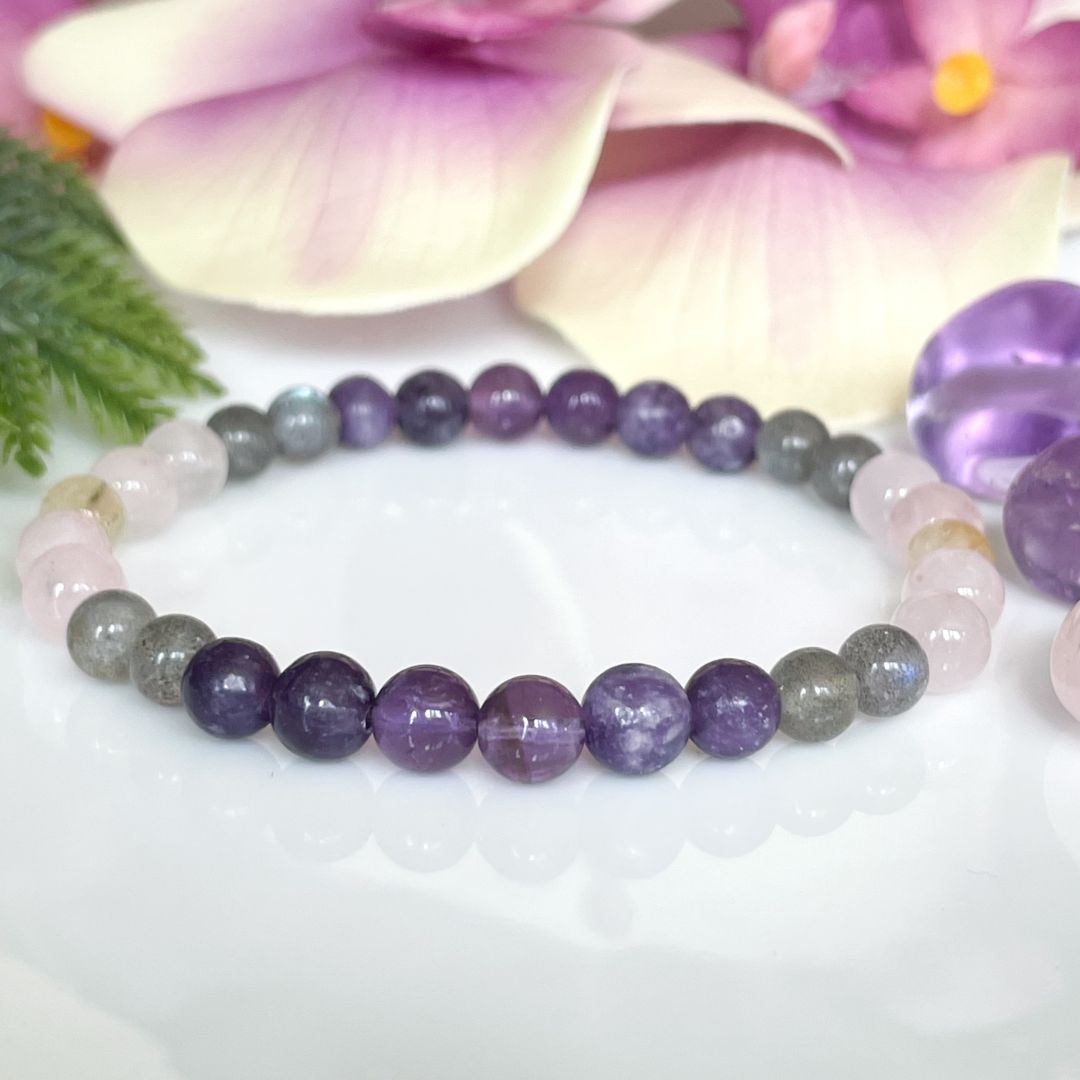 Beaded bracelet with purple and gray stones on a white background with flowers.