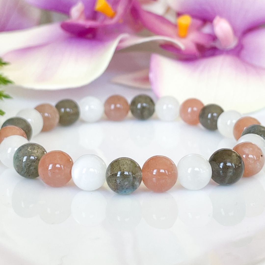 Beaded bracelet with multicolored beads on a white surface with purple flowers in the background